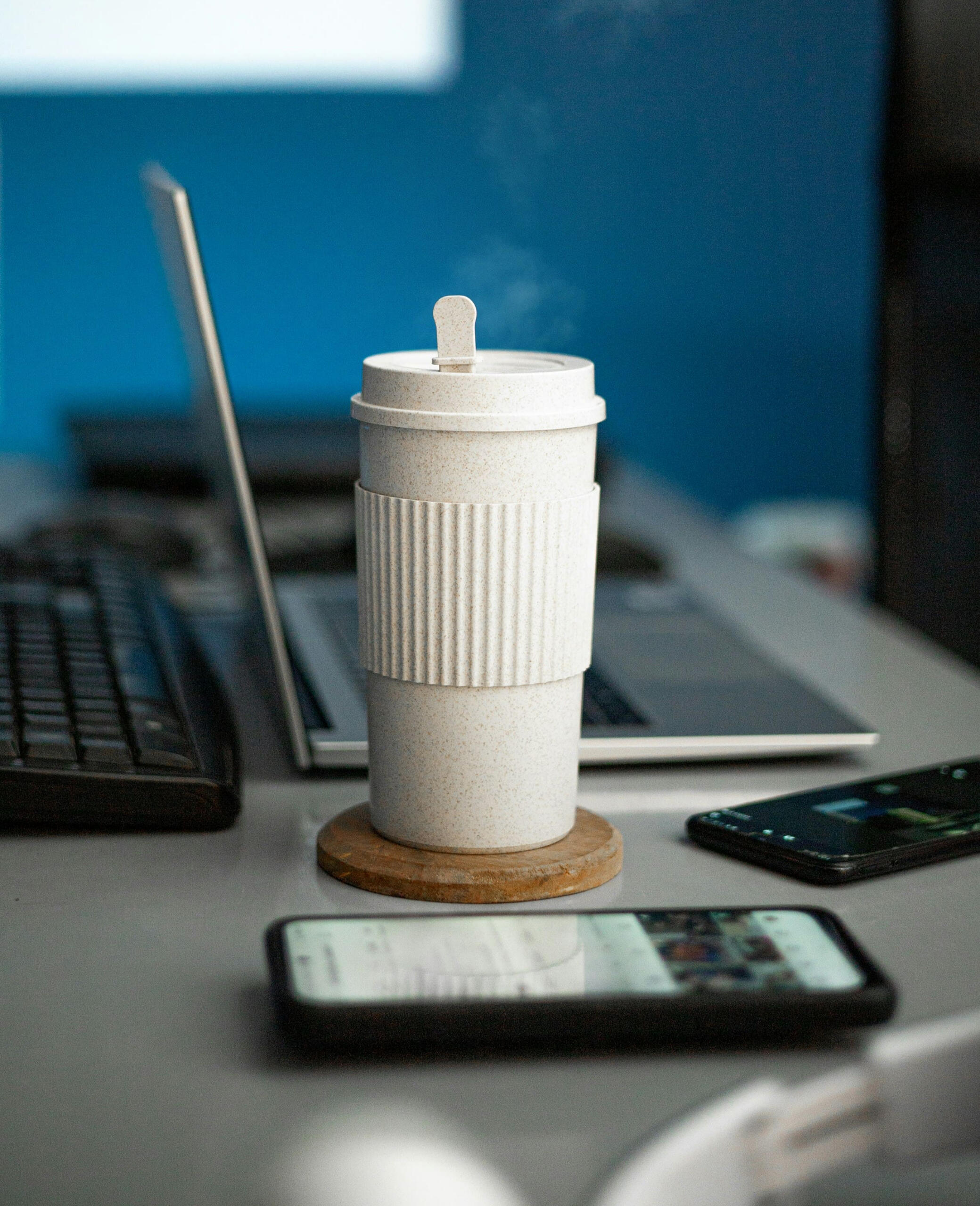 A coffee cup on a desk beside a laptop and smartphone, symbolizing work and digital tools
