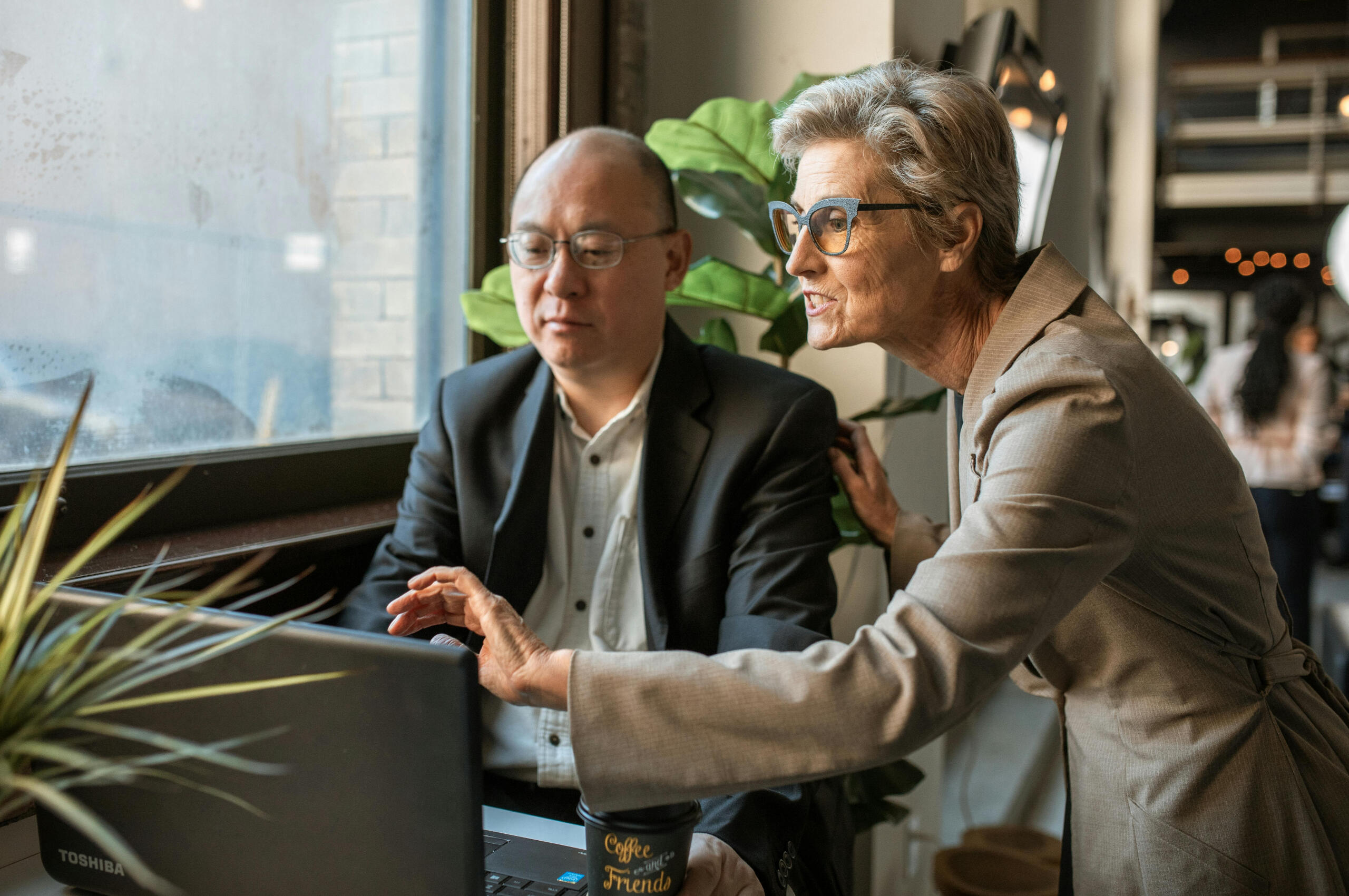 Workforce and community partnership collaboration A professional guiding a colleague at a laptop, symbolizing Brasstown Consulting’s partnerships with workforce boards and community organizations to build digital confidence and support real job skills